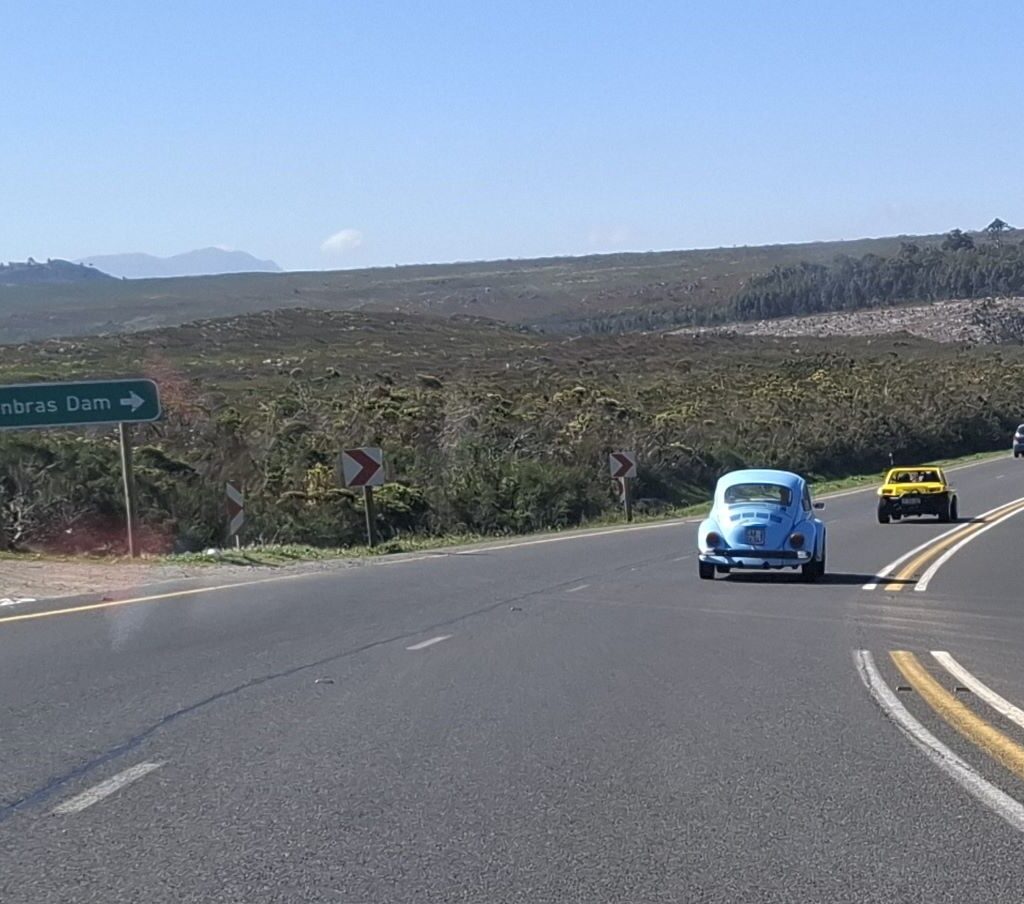 A convoy of VW Air cooled vehicles, including a VW Beach Buggy and a VW Beetle, driven by Anthony, Fabian, and Kyle, cruising along a scenic mountain road.