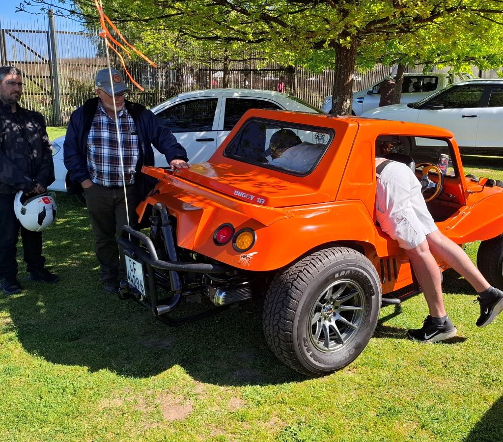 Brent is seen with his legs hanging out of his VW Beach Buggy, "The Wasp," as he works on a repair or adjustment.