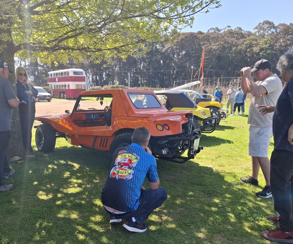 Members of the Wild Buggers club are gathered on a lawn under the trees, chatting and relaxing during their run.