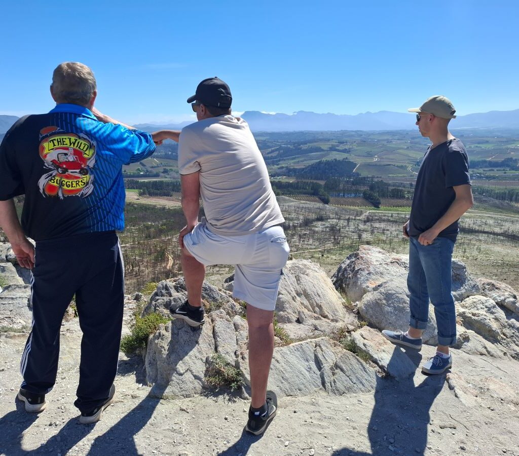 Chris, Brent, and Kyle stand on the edge of a precipice, looking at the stunning view after their drive on the Highlands Road.