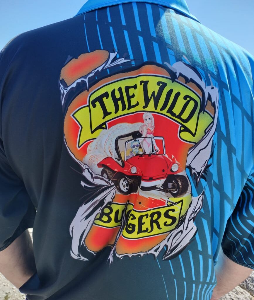 The back of Chris's club shirt is visible, showing the Wild Buggers logo as he stands on the edge of a scenic lookout point.