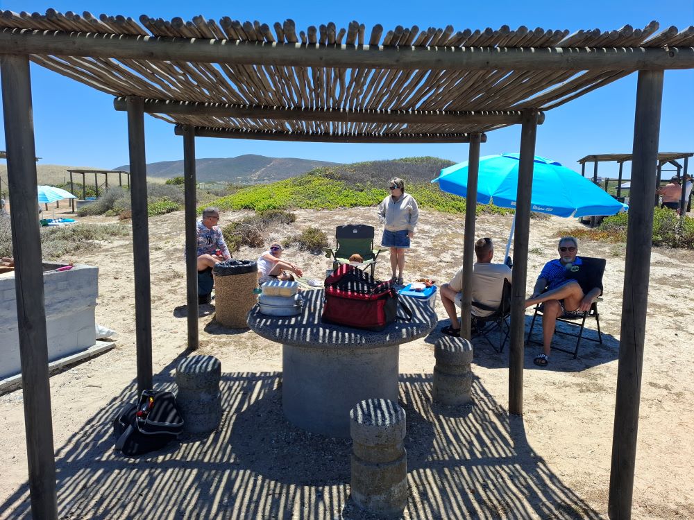 The Wild Buggers crew relaxing under the afdakkie at the braai area, their Beach Buggy and VW air cooled fleet parked nearby at Eerste Steen.