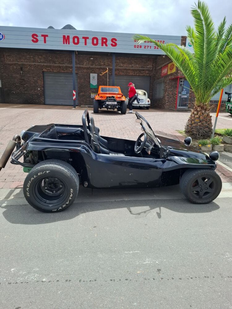 A black Beamish beach buggy parked in front of ST Motors in Hermanus, with an orange Salamander beach buggy parked further back in the workshop area.