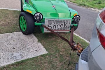 The green Kango beach buggy "Shrek" with a Nissan water-cooled engine, showing a wet patch on the pavement from a blown head gasket, followed by a photo of Shrek being towed by an A-frame on a suburban street.