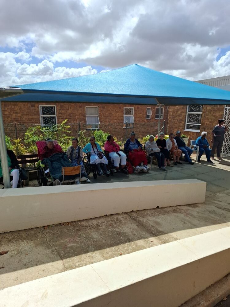 Residents of the Badisa Goue Aar home for the elderly watching the Wild Buggers Beach Buggy Club charity event from under a blue shade port.