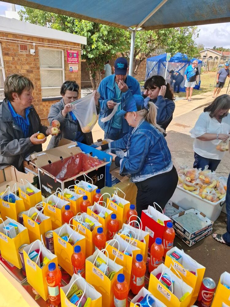 Alt Text: Wild Buggers Beach Buggy Club "Ladybugs" and volunteers packing fruit and care parcels for the elderly at Badisa Goue Aar.