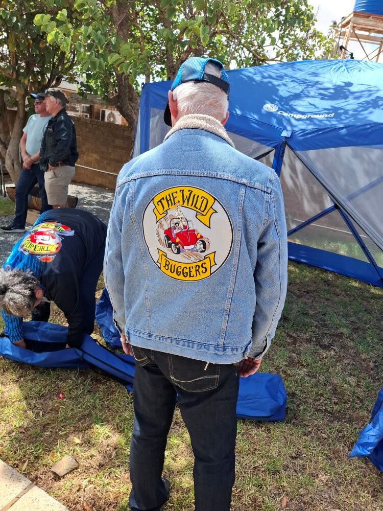 A member of The Wild Buggers Beach Buggy Club wearing a denim jacket with the club logo while setting up a blue gazebo for the charity event.