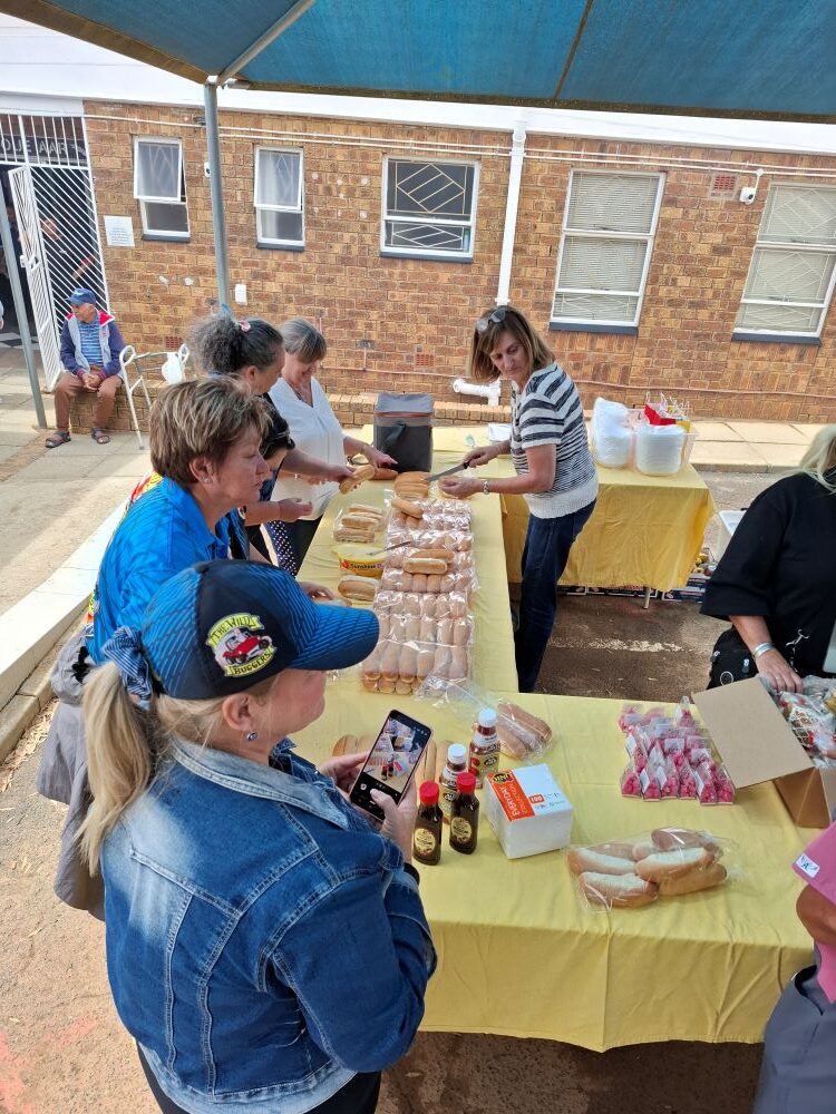 Wild Buggers "Ladybugs" and volunteers preparing hot dog rolls for a boerewors roll lunch at the Goue Aar home.