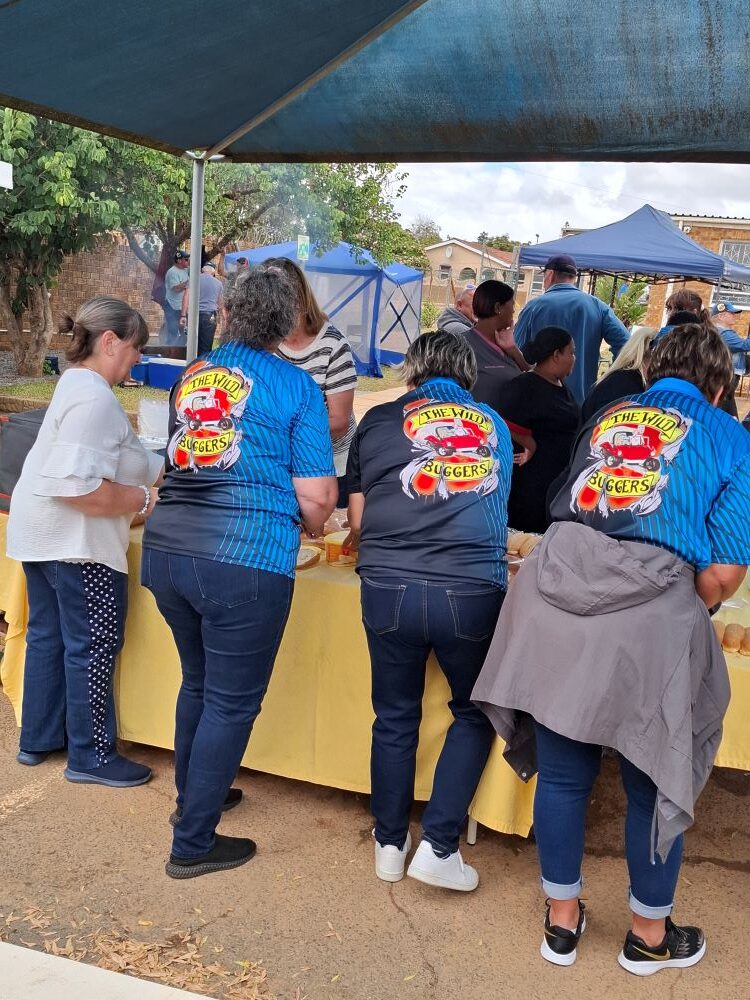 A back-view of Wild Buggers club members wearing their official blue and black club shirts while preparing food at the Goue Aar charity event.