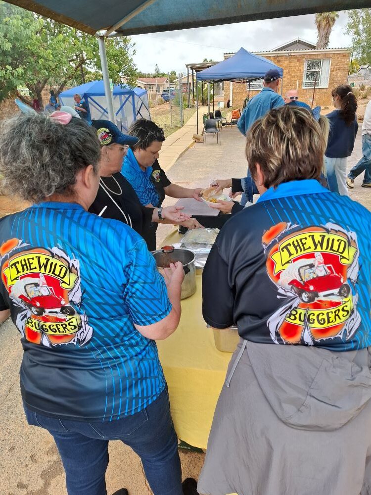 Mickey and Sandra from The Wild Buggers Beach Buggy Club wearing official branded club shirts while serving food at a charity event in Malmesbury.