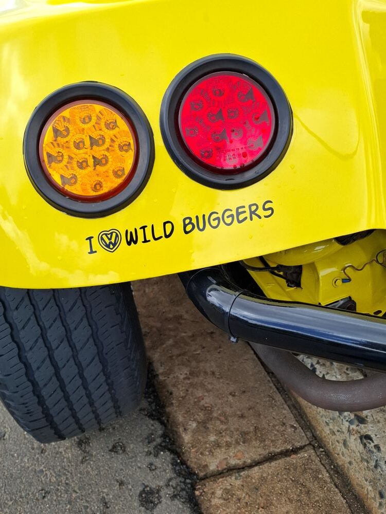 A close-up of the yellow rear fender of a beach buggy featuring circular taillights and an "I ❤️ VW WILD BUGGERS" sticker.