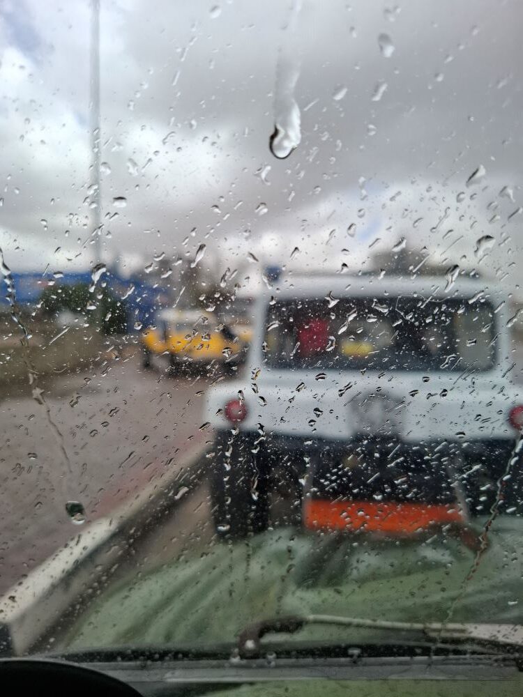 Raindrops on a windshield looking out at a white and yellow beach buggy convoy during a Wild Buggers club run.