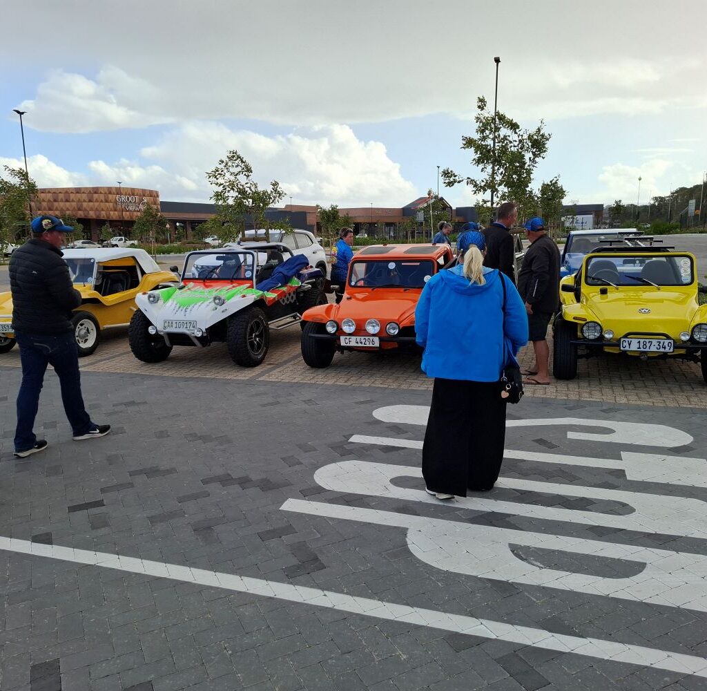 A colorful convoy of beach buggies, including yellow, orange, and white models, parked in a shopping center lot after The Wild Buggers charity event.
