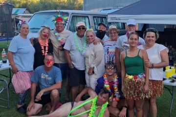 Members of the Wild Buggers Beach Buggy Club in various costumes, including a Borat mankini, unicorn, elf, and headdress, gathered around a braai fire at Die Hut campsite.