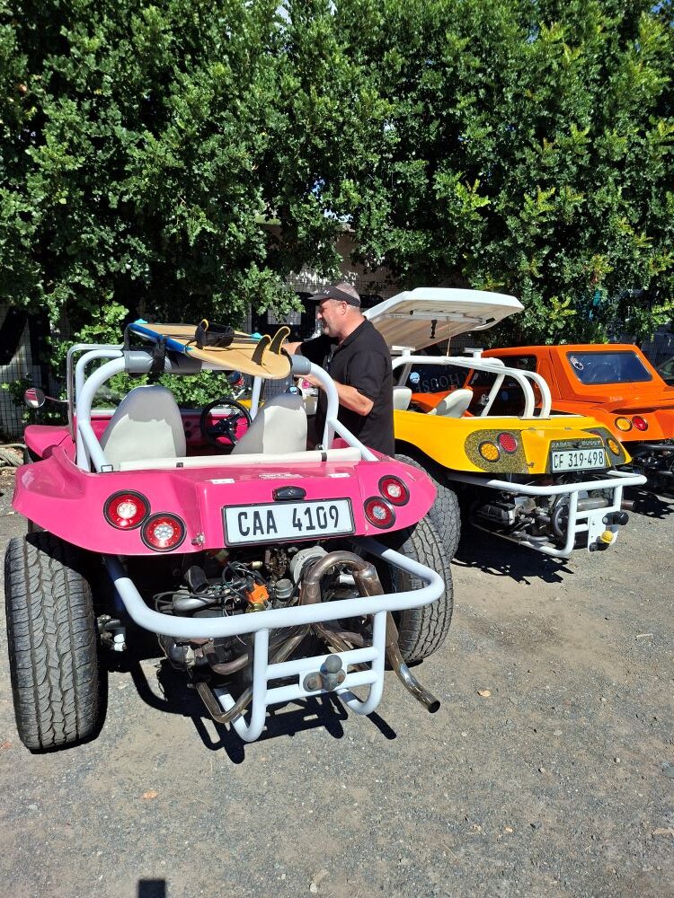 A side profile view of Morris Munitz’s unique pink Beamish beach buggy with a surfboard on the roof, parked at Oceana Power Boat Club in Cape Town.