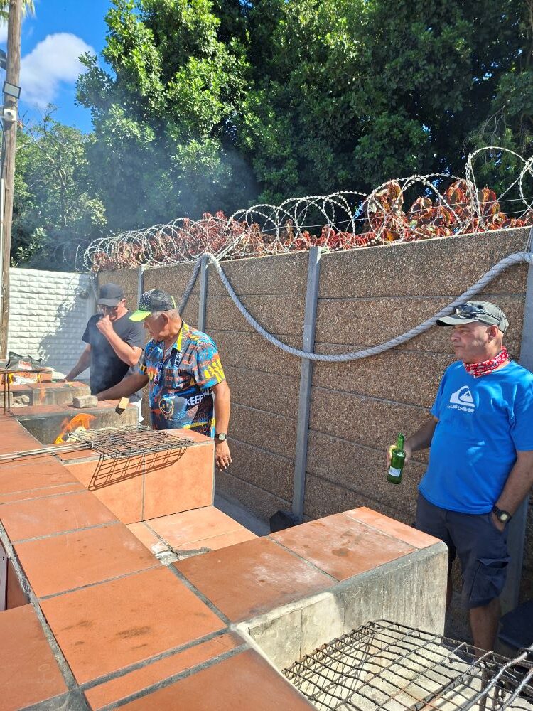 Wild Buggers Beach Buggy Club members standing around a brick braai area preparing food at the Oceana Power Boat Club.