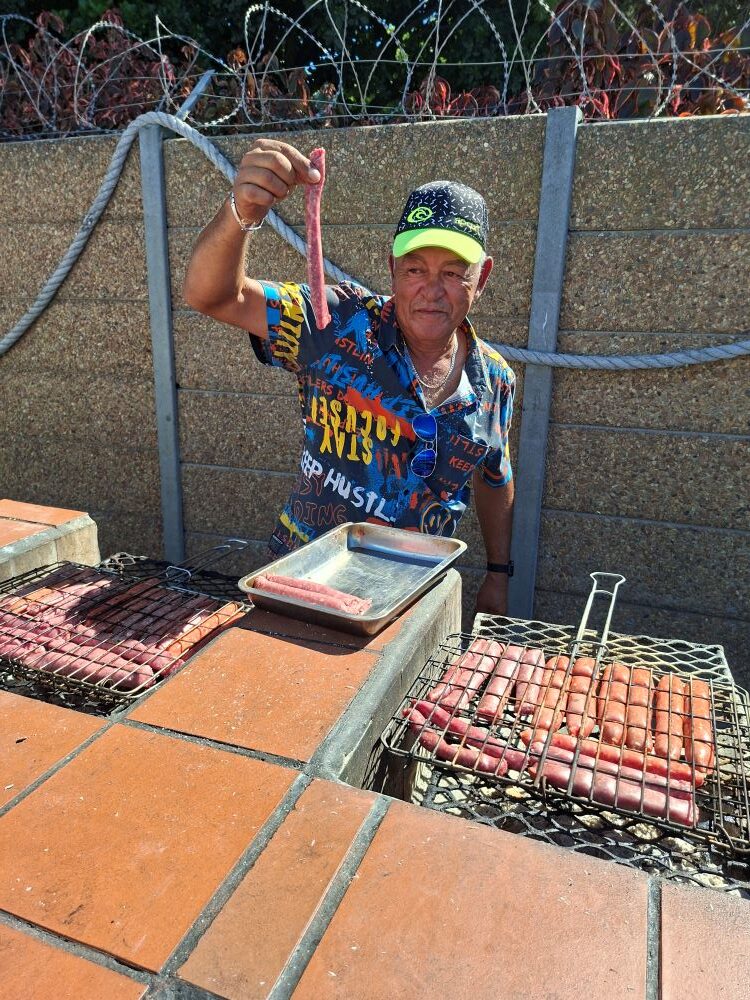 Faizal, a member of the Wild Buggers Beach Buggy Club, holding up a piece of boerewors over a hot braai at the Oceana Power Boat Club.