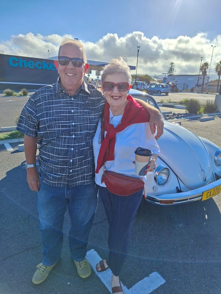 Wild Buggers club members Andre and Jo-ann posing with coffee in front of their classic white VW Beetle at Bothasig Square.