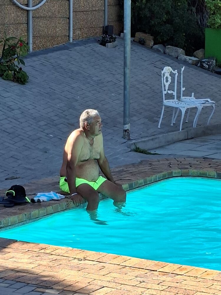 Wild Buggers Beach Buggy Club member Faizal sitting on the edge of a sparkling blue swimming pool at the Oceana Power Boat Club.