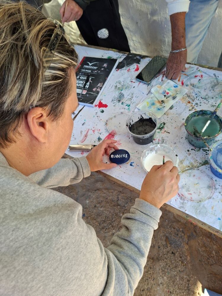 Yolande painting the word ‘Buggers’ on a stone at !Khwa ttu during the Wild Buggers West Coast cultural experience Run, where painted stones are placed into a large Africa-shaped ground artwork at the San Heritage Centre.