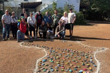 Wild Buggers members posing for a group photo at the Africa-shaped stone artwork at !Khwa ttu during the West Coast cultural experience Run, surrounded by the painted stones added at the San Heritage Centre.