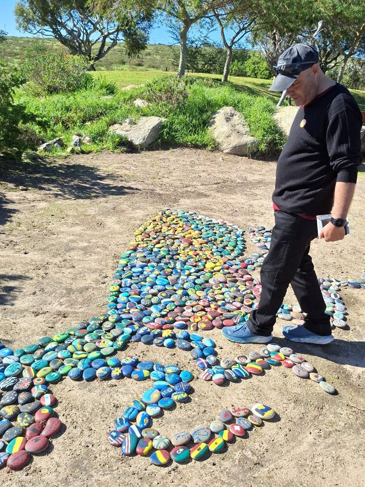 Wiehann looking at painted stones laid out in the shape of a huge praying mantis at !Khwa ttu during the Wild Buggers West Coast cultural experience Run, highlighting a creative outdoor display at the San Heritage Centre.