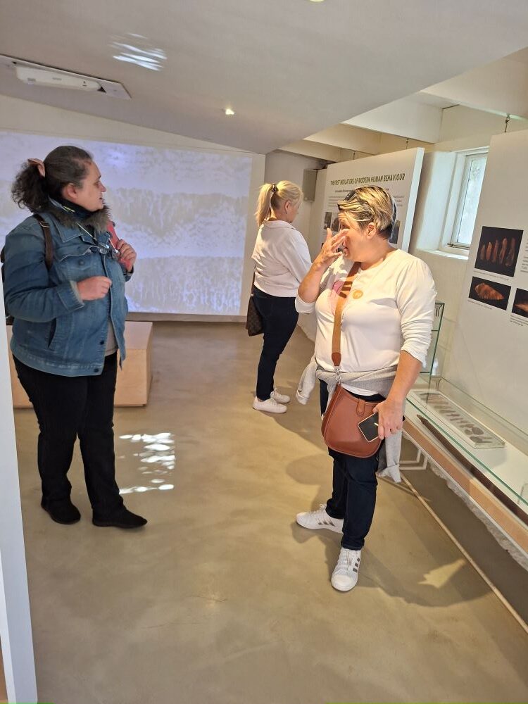 Yolande and Mickey standing together and chatting inside one of the main exhibition halls at !Khwa ttu during the Wild Buggers West Coast cultural experience Run at the San Heritage Centre.