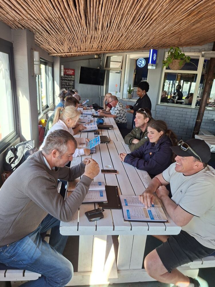 Wild Buggers club members sitting together around a large table at the Seafood Lapa restaurant in Melkbosstrand, looking at menus and preparing to order lunch.