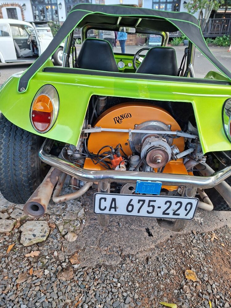 A close-up rear view of Dan Laarman’s metallic green classic VW beach buggy named Rango, showing an exposed 1600 air-cooled Beetle engine with a bright orange fan shroud, chrome bumper, custom exhaust, and a Cape Town registration plate at a car club meeting point.