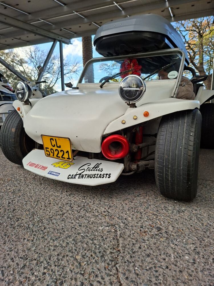 A custom white Beamish beach buggy featuring a large grey Thule roof box mounted on the roll bar, a exposed 1600 twin-port air-cooled VW engine, wide rear tyres, and a Stellenbosch license plate, parked at a car club event meeting point.