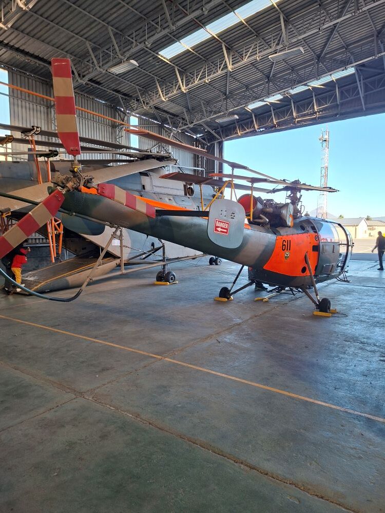 A vintage Sud Aviation SA 316B Alouette III helicopter with tail number 611 on static display inside a hangar at the South African Air Force Museum during a classic car run.