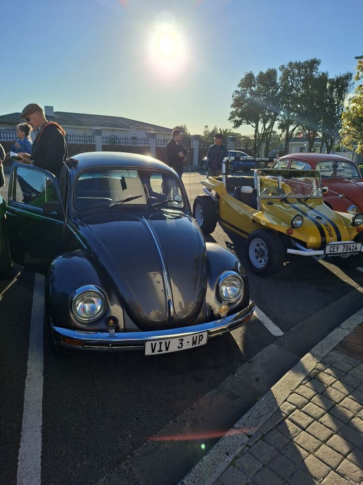 A custom metallic gunmetal grey 1600 VW air-cooled Beetle parked next to a yellow beach buggy at the Woodbridge Island meeting point for a classic car run.