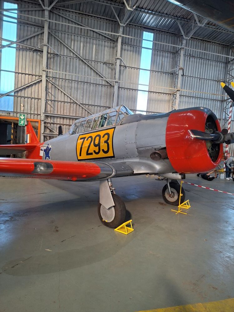 A vintage North American Harvard trainer aircraft with tail number 7293 on display inside a hangar at the South African Air Force Museum during a classic car club run.