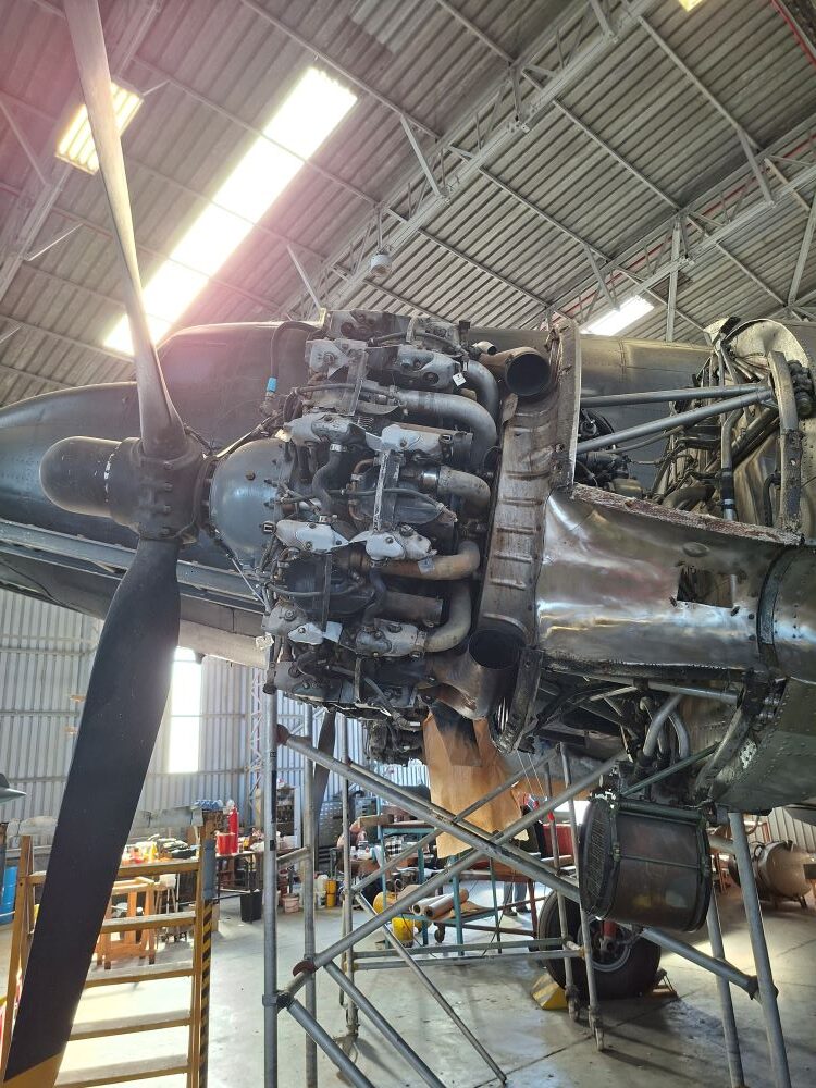 A detailed view of an exposed twin row radial engine and propeller assembly undergoing restoration inside the workshop hangar at the South African Air Force Museum during a classic car club run.