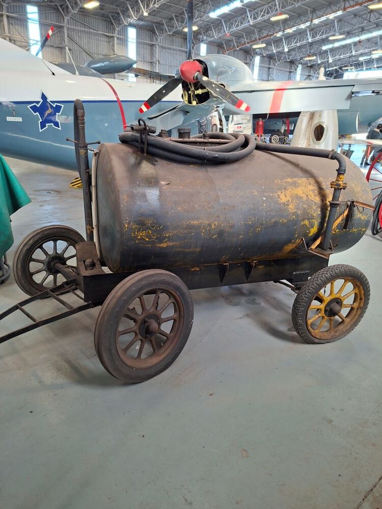 A vintage mobile airfield fuel bowser tank cart on spoked wheels inside the South African Air Force Museum hangar during a Wild Buggers club event for custom beach buggies, Baja Bugs, and classic VW air-cooled vehicles.