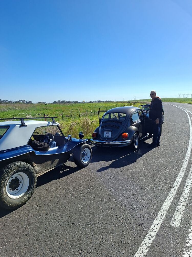A blue beach buggy and a gunmetal grey VW Beetle parked on the side of a country road as a club member prepares to depart on the Propellers and Pistons Winter Cruise featuring classic VW air-cooled vehicles.
