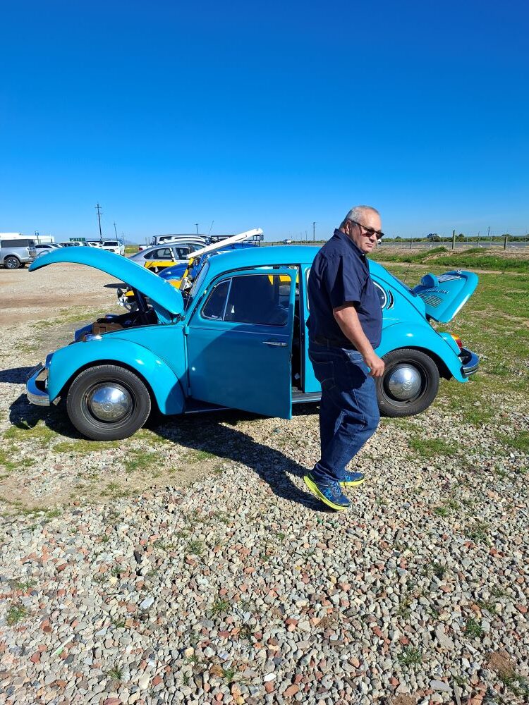 A turquoise blue classic VW air-cooled Beetle with its hood and engine lid open for cooling during an unexpected maintenance stop at De Werf during a Wild Buggers club event featuring custom beach buggies and Baja Bugs.