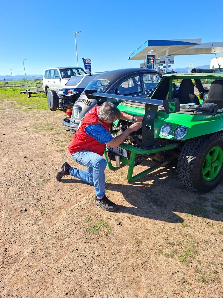 A club member performing a quick roadside repair on a green custom beach buggy named Shrek during the Propellers and Pistons Winter Cruise, an event showcasing classic VW air-cooled vehicles and Baja Bugs.