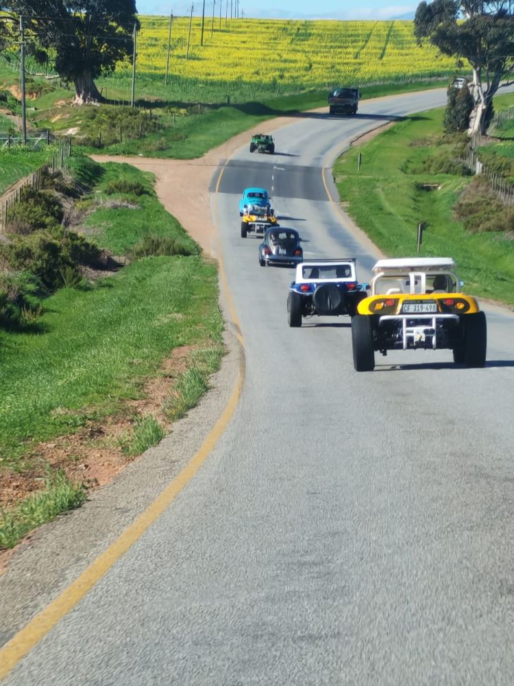 A convoy of custom beach buggies, Baja Bugs, and classic VW air-cooled vehicles traveling in a line along a winding country road during the Wild Buggers club Propellers and Pistons Winter Cruise.