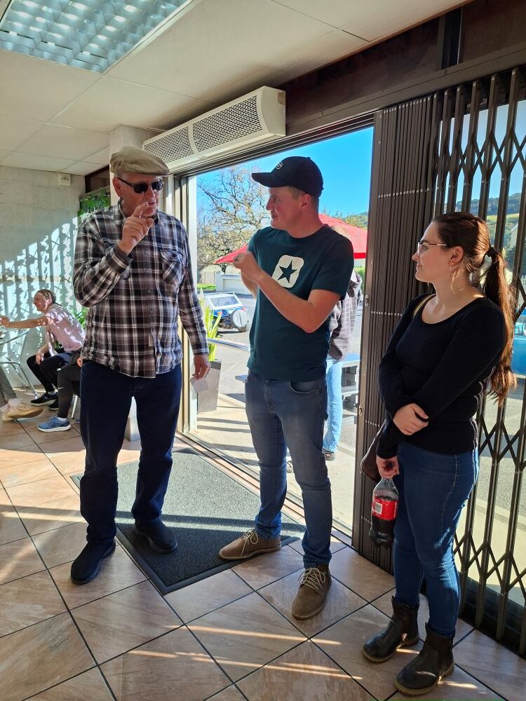 Club members Viv and Pieter chatting with a guest while waiting for their food orders at Cape to Rio Fisheries during the Wild Buggers Beach Buggy Club Propellers and Pistons Winter Cruise, an event featuring custom beach buggies, Baja Bugs, and classic VW air-cooled vehicles.