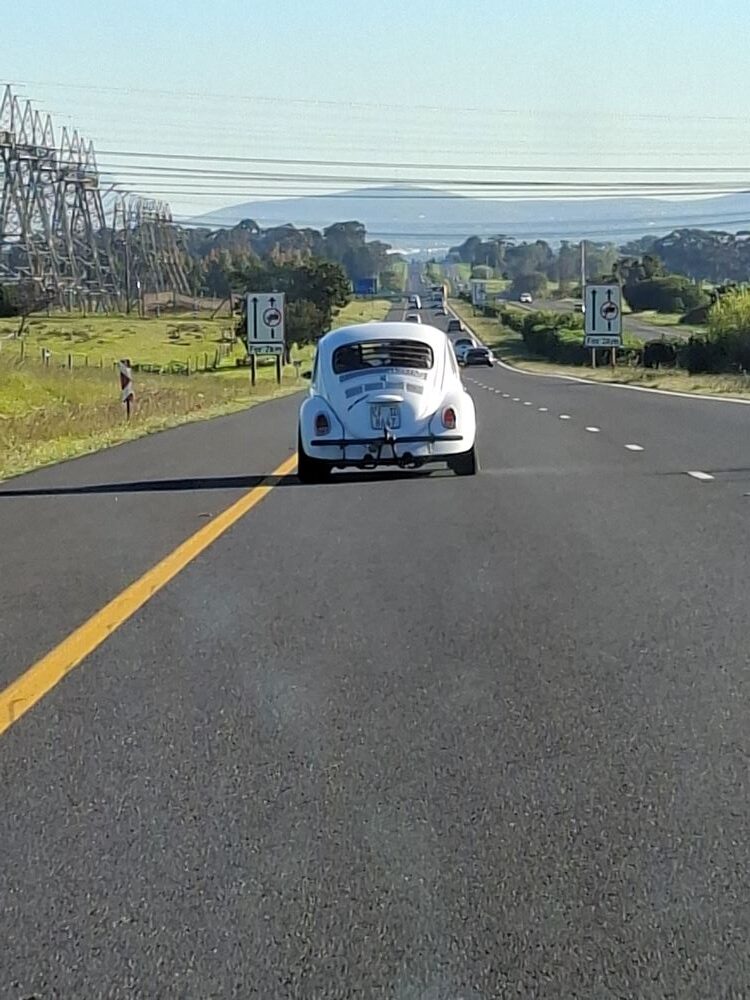 A view from the road as a classic VW air-cooled Beetle leads the way back towards Cape Town on the N1 highway after the Propellers and Pistons Winter Cruise, an event featuring custom Beach Buggy and Baja Bug vehicles.