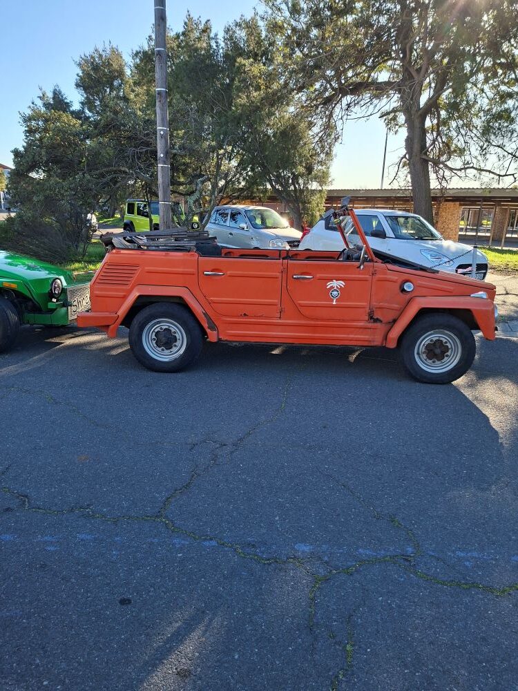 A classic orange VW Type 181 Thing parked in a lot next to a green beach buggy during the Wild Buggers club run to the SAAF Museum.