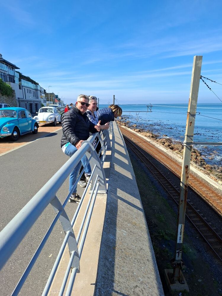 Wild Buggers club members enjoying the beautiful ocean view alongside parked classic VW air-cooled vehicles during the From Bars to Battleships run.