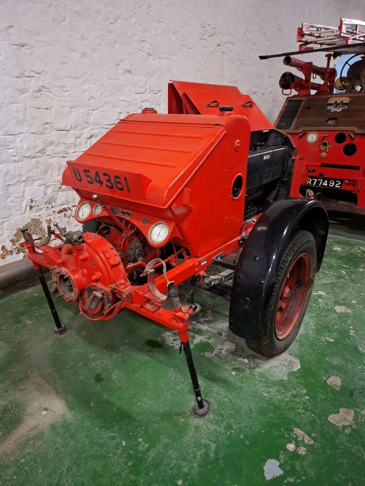 A vintage portable fire pump trailer on display alongside a historical fire engine inside the museum.