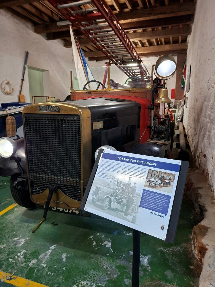 A restored Leyland Cub fire engine on display with its informational plaque inside the South African Naval Museum.