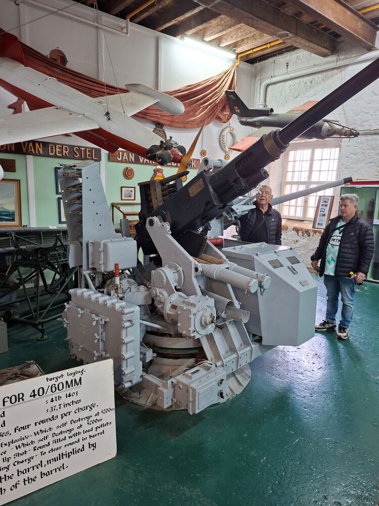 Club members examining a historical 40 mm naval anti-aircraft gun exhibit with target laying plaque inside the museum.