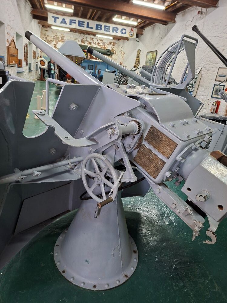 A restored naval deck gun with elevation handwheels and a protective shield on display inside the museum.