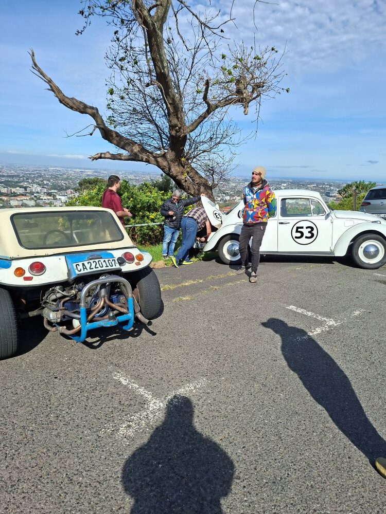 Club members chatting and looking at a beach buggy and a classic VW Beetle at Rhodes Memorial while dealing with a stubborn backfiring issue.