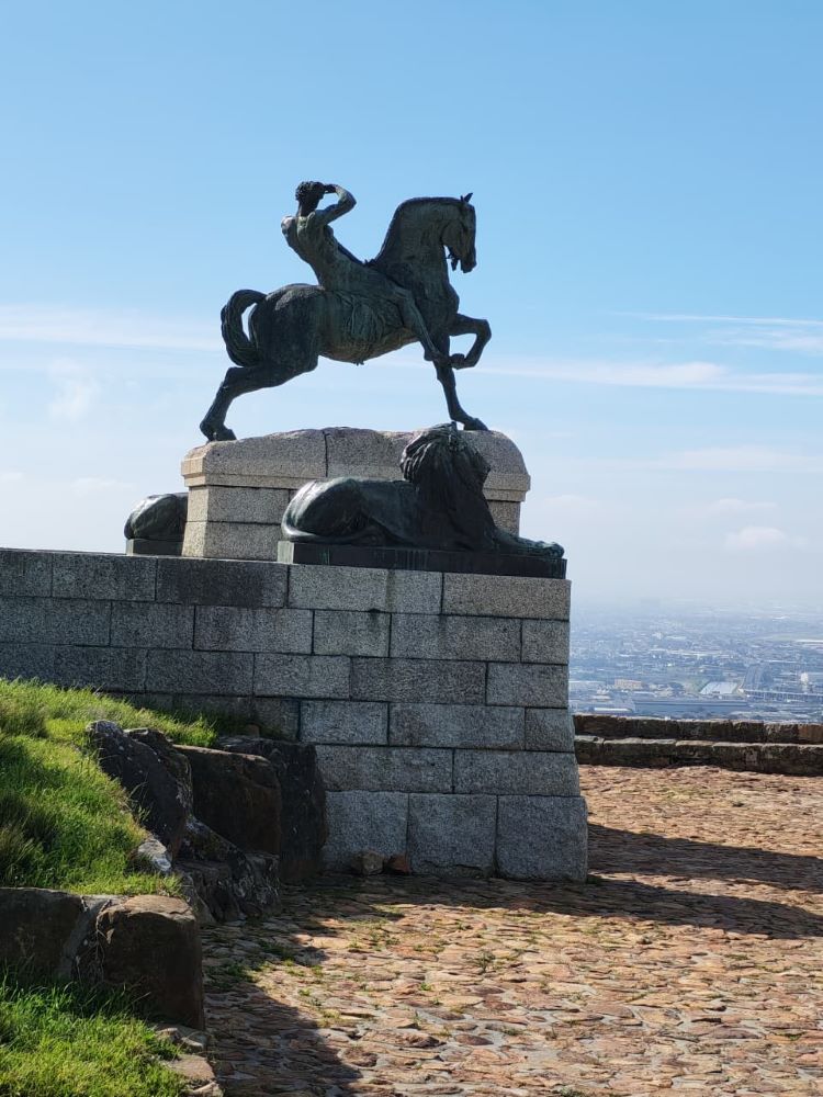 The iconic bronze horse and rider statue standing guard at Rhodes Memorial under a clear blue sky.