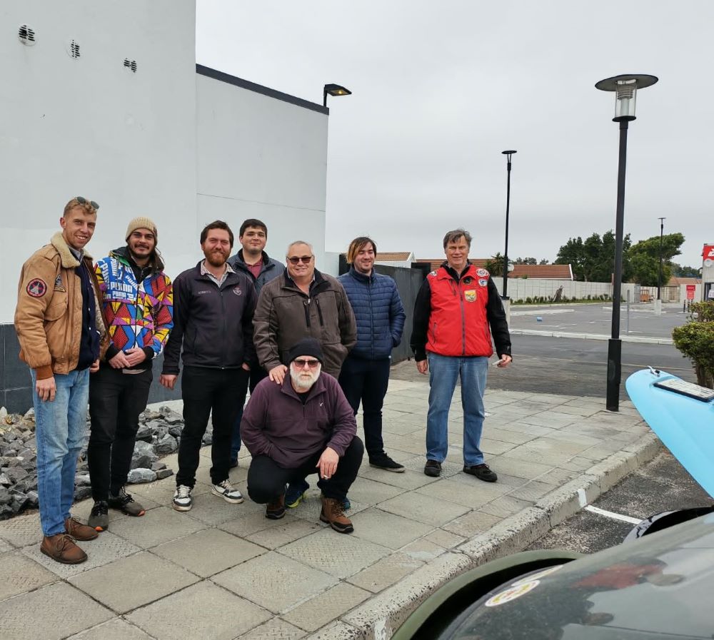 Club members gathering for a group photo alongside classic VW air-cooled vehicles and a beach buggy at the morning meetup before the From Bars to Battleships run.